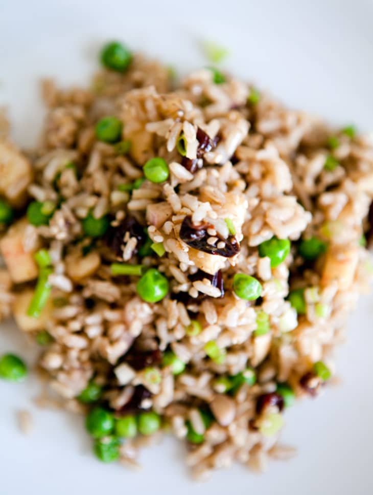 Brown rice mixed with peas, raisins, and chopped nuts on a white plate.