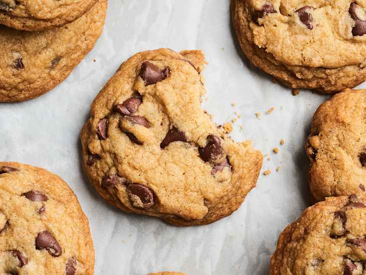 Chocolate chip cookies on parchment paper, one cookie with a bite taken out, surrounded by whole cookies.