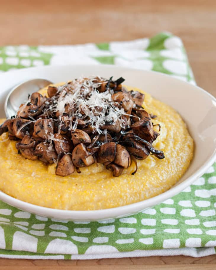 Creamy polenta topped with sautéed mushrooms and grated cheese in a white bowl on a patterned napkin.