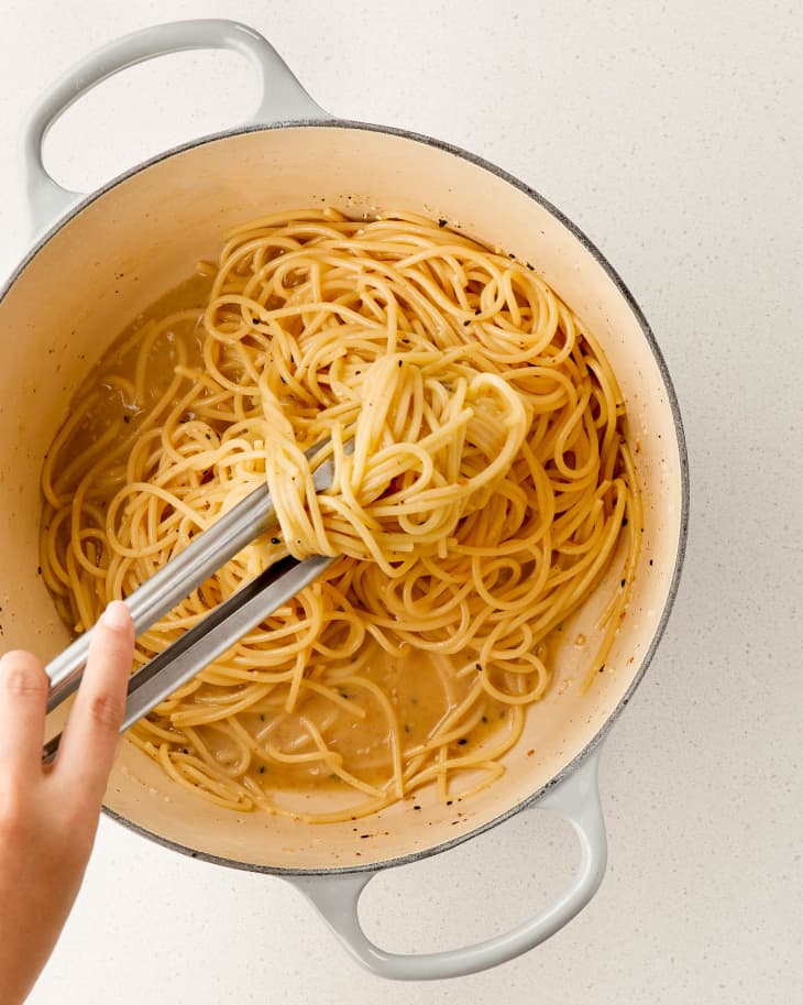 Spaghetti carbonara in a pot with creamy sauce, stirred with tongs.