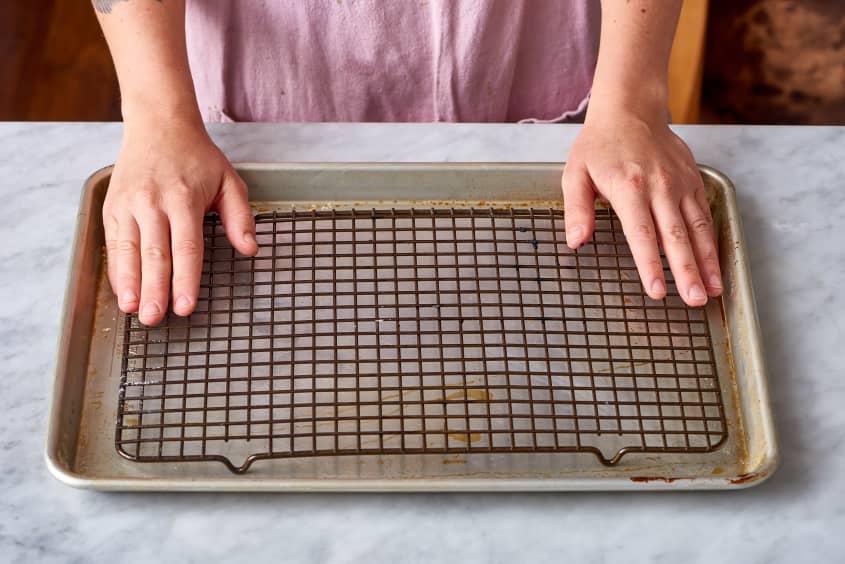 Hands placing a wire rack on a baking sheet, preparing for oven-baked chicken.
