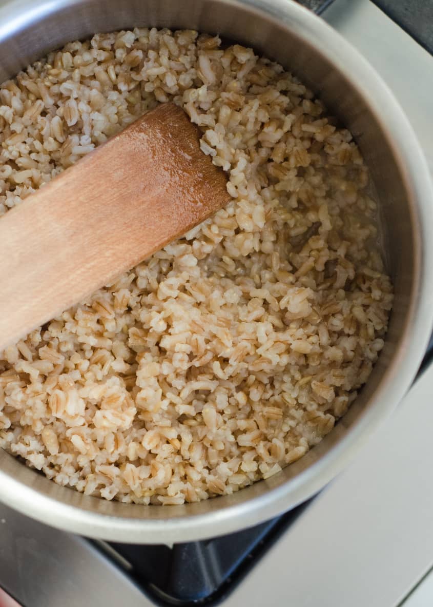 Cooked brown rice in a pot with a wooden spatula on a stovetop.