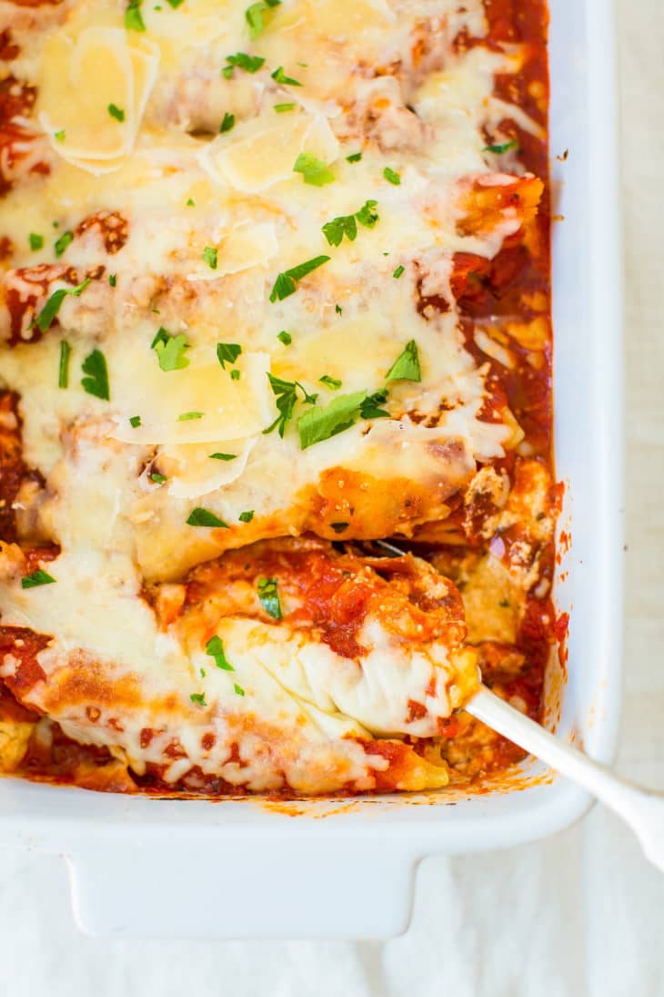 Baked manicotti with melted cheese, sun-dried tomatoes, and fresh thyme in a white baking dish.