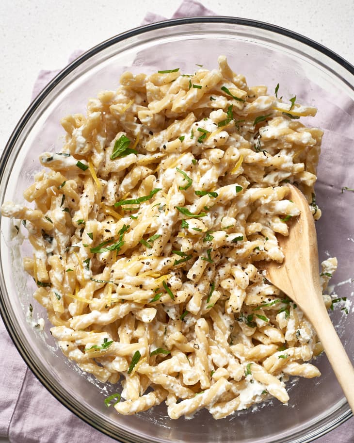 Pasta with ricotta, lemon zest, and basil in a glass bowl, mixed with a wooden spoon.