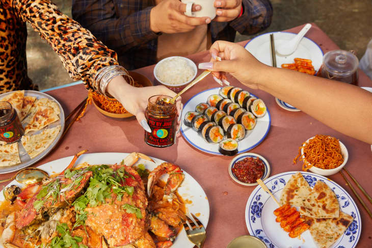 Table with spicy crab, sushi rolls, flatbread, and chili sauce, surrounded by people sharing a meal.