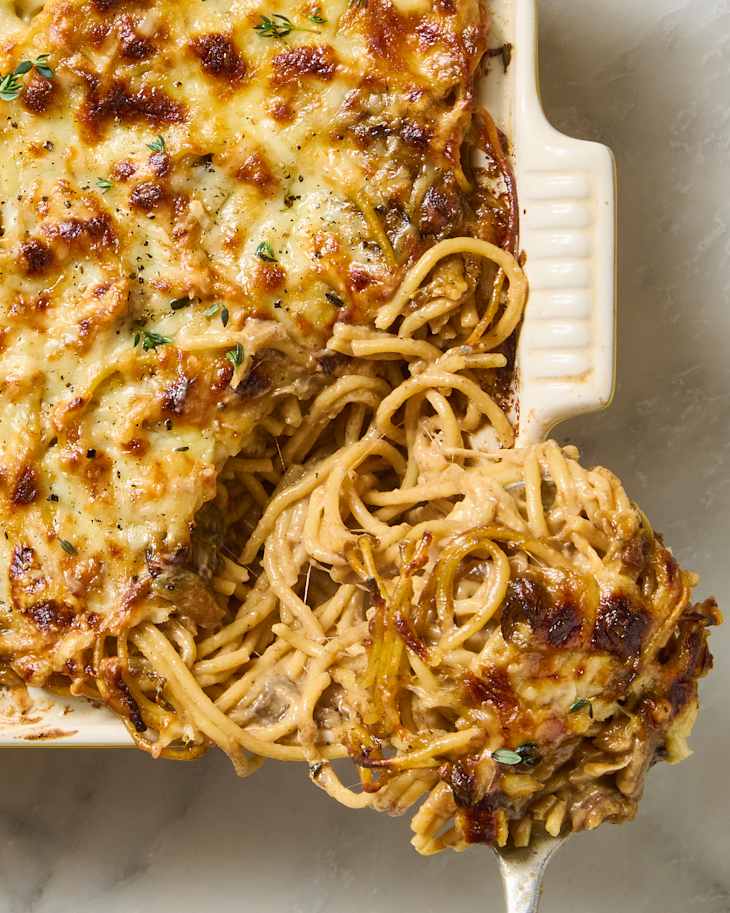 Creamy baked spaghetti with a golden, cheesy crust and fresh thyme on top, served in a baking dish.
