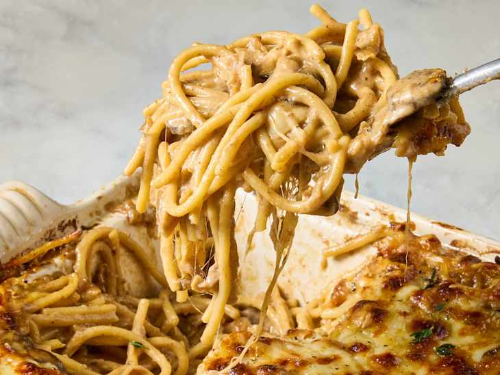 Creamy baked spaghetti being lifted from a dish, with melted cheese and a golden crust.