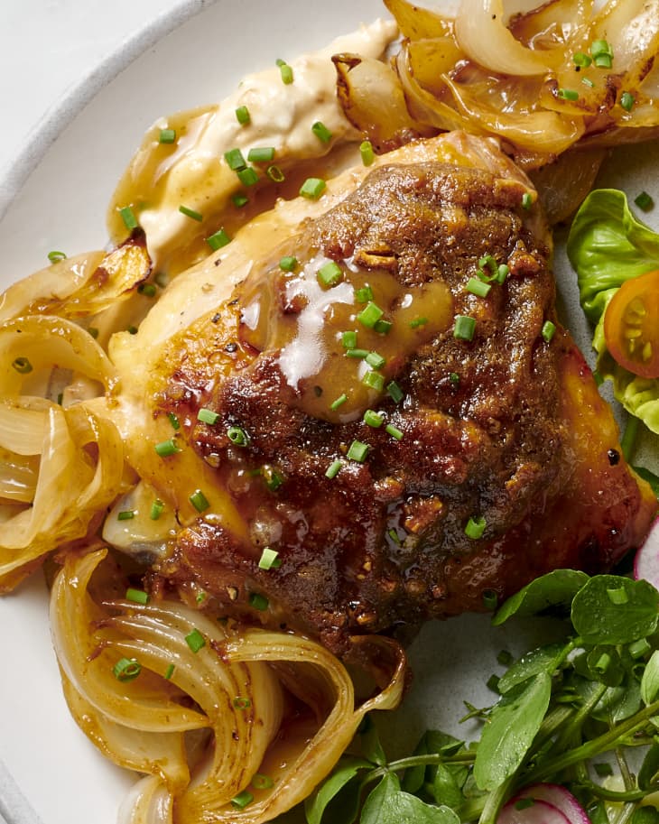 a plated chicken thigh resting on a bed of cooked onions and French onion dip with a small side salad