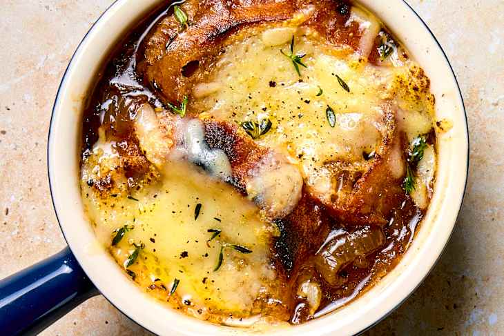 Overhead shot of french onion soup in a navy blue soup crock, topped with herbs.