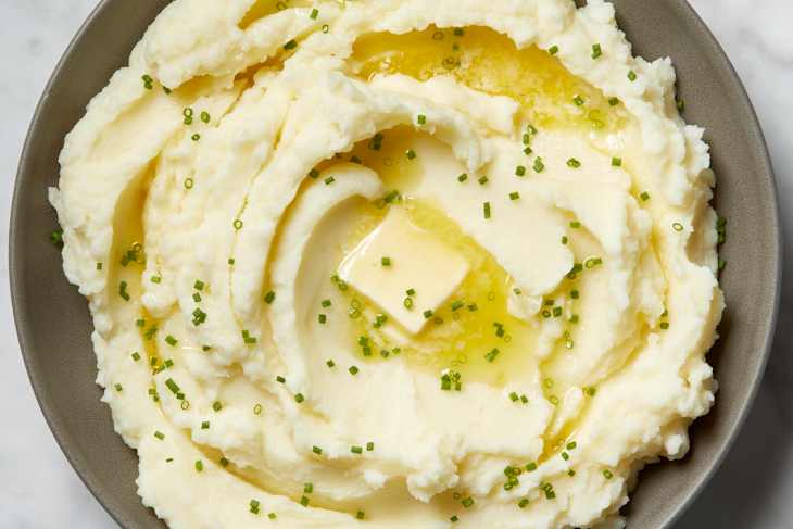Overhead view of mashed potatoes in a grey bowl, topped with chives and a pat of butter.
