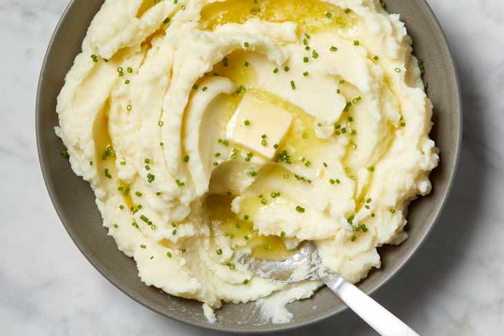 Overhead view of mashed potatoes in a grey bowl, topped with chives, a pat of butter and a spoon in the bowl.