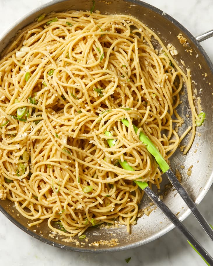 Overhead view of garlic noodles in a silver pan with tongs resting in it.