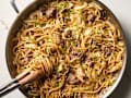 Stir-fried noodles with ground beef and cabbage in a large skillet, mixed with a wooden utensil.