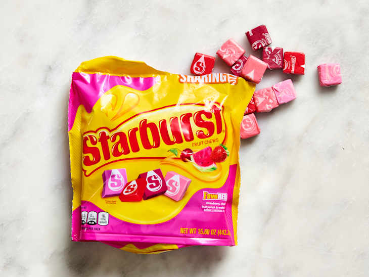 Opened bag of Starburst fruit chews with pink and red candies scattered on a light surface.