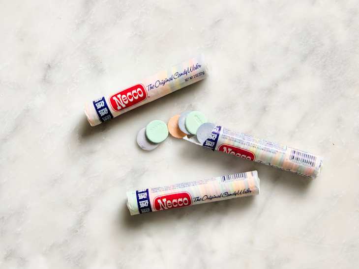 Three rolls of Necco wafers with pastel-colored candies scattered on a light marble surface.