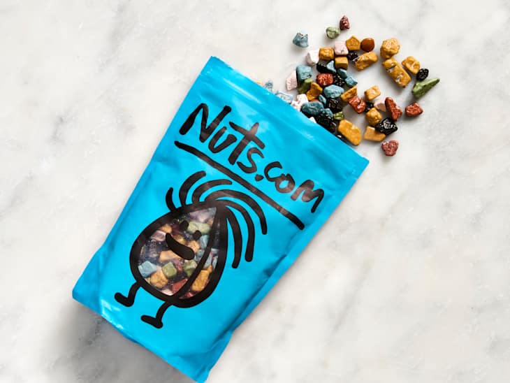 Colorful candy pieces spilling from a blue bag with a cartoon character design and "Nuts.com" label.