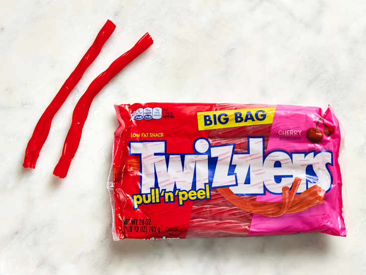 Red Twizzlers pull 'n' peel candy sticks next to a large pink bag labeled "Twizzlers" with cherry flavor.