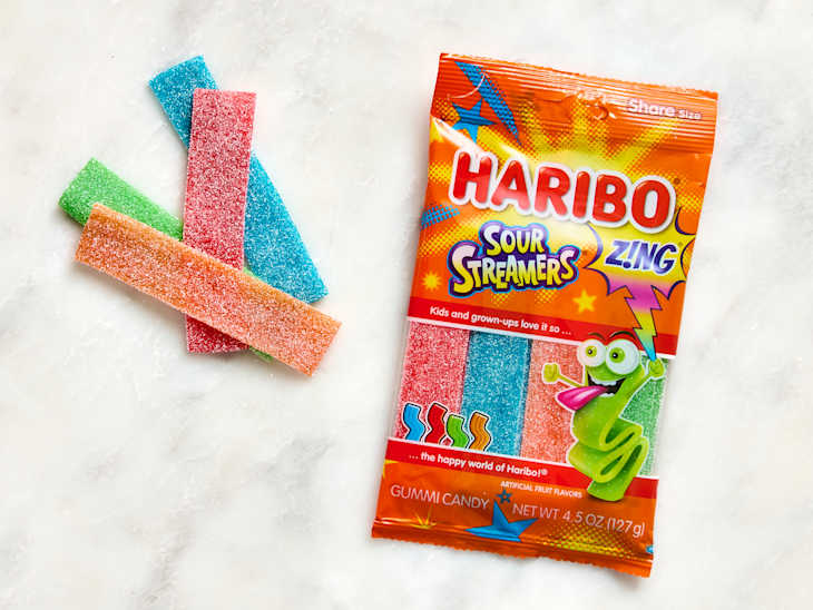 Colorful sour gummy candy strips in red, blue, green, and orange, next to a vibrant Haribo Sour Streamers package.