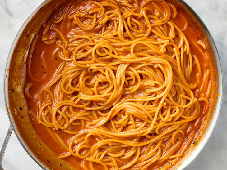 Spaghetti coated in a rich, creamy tomato sauce with black pepper, in a stainless steel pan.