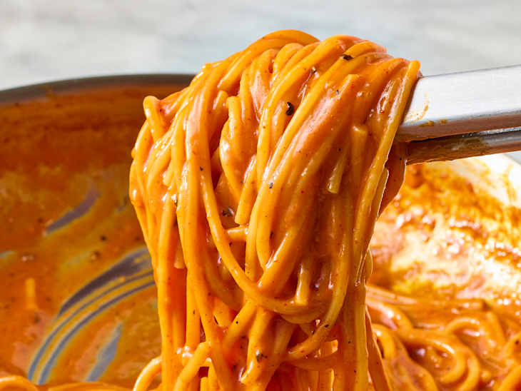 Spaghetti coated in a rich orange sauce, being lifted from a pan.
