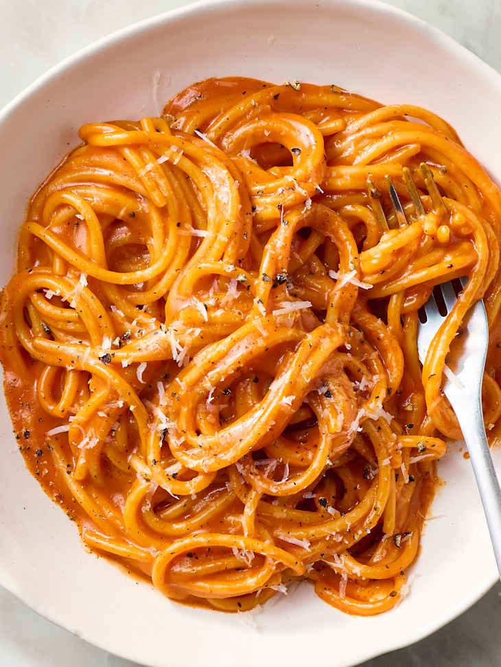 Creamy pasta dish with orange sauce, topped with grated cheese and black pepper, served in a white bowl.