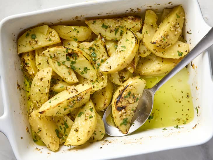 overhead shot of greek lemon potatoes in a white baking dish, and a large serving spoon resting in the dish