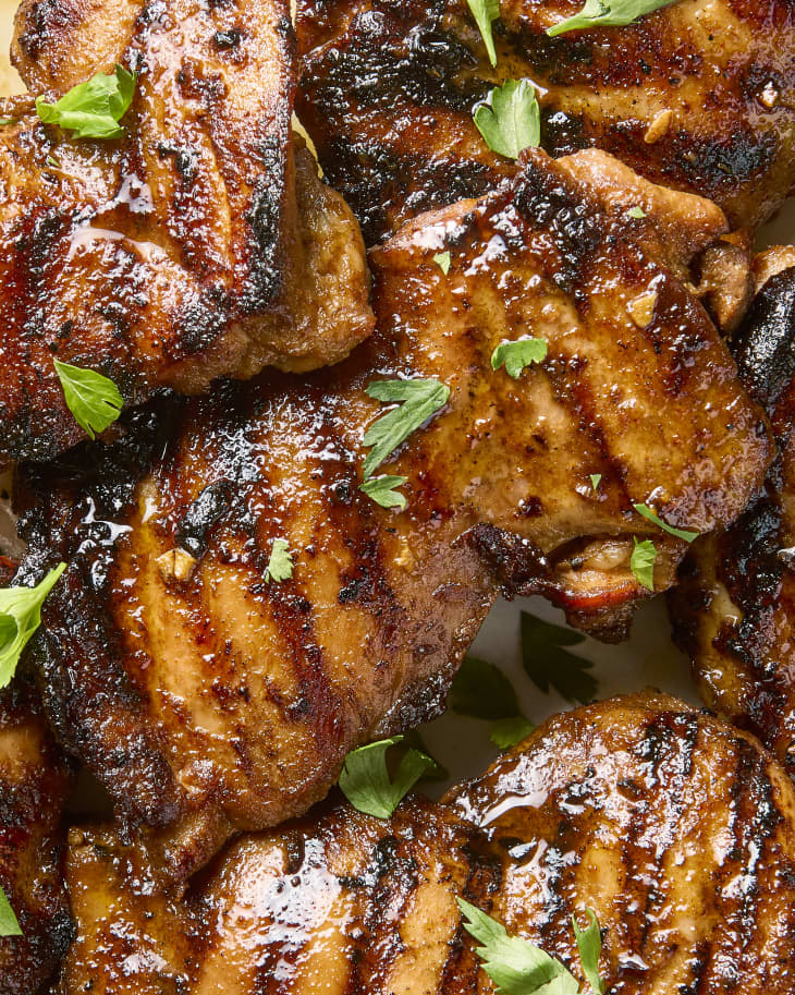overhead shot of grilled chicken thighs on a platter, topped with herbs