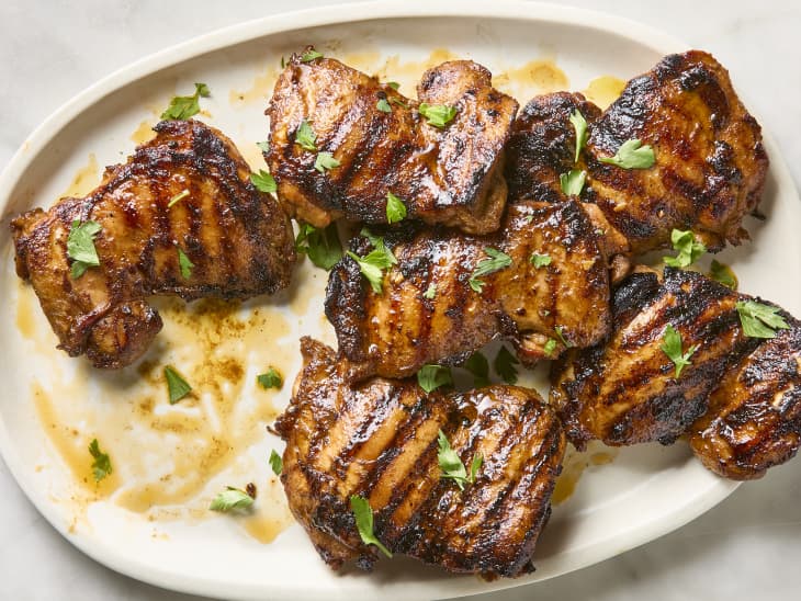 overhead shot of grilled chicken thighs on a platter, topped with herbs