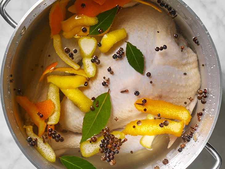Overhead view of brine ingredients in a silver pot full of water covering the turkey.