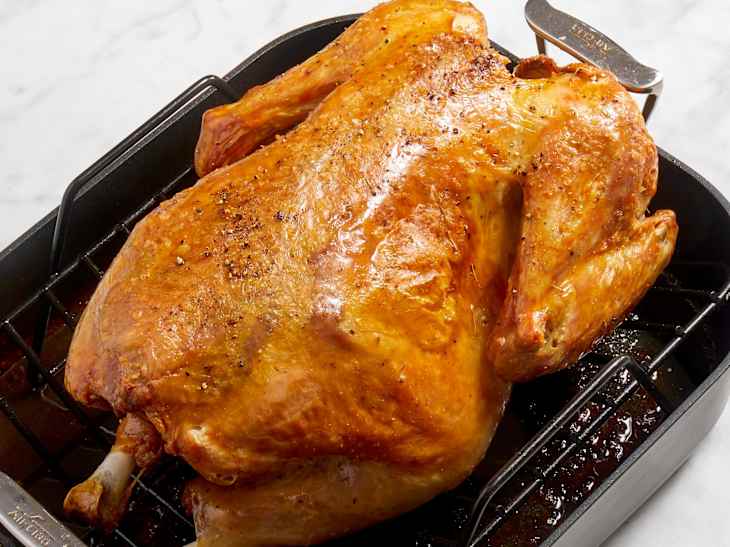 Angled view of a whole roasted turkey in a black pan.