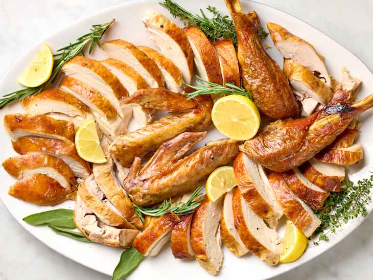 overhead shot of a fully carved thanksgiving turkey on a platter with herbs and lemon