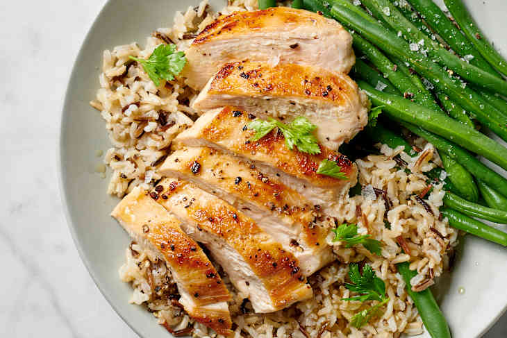 a sliced moist and tender chicken breast with a perfect sear on a bed of wild rice and a side of green beans