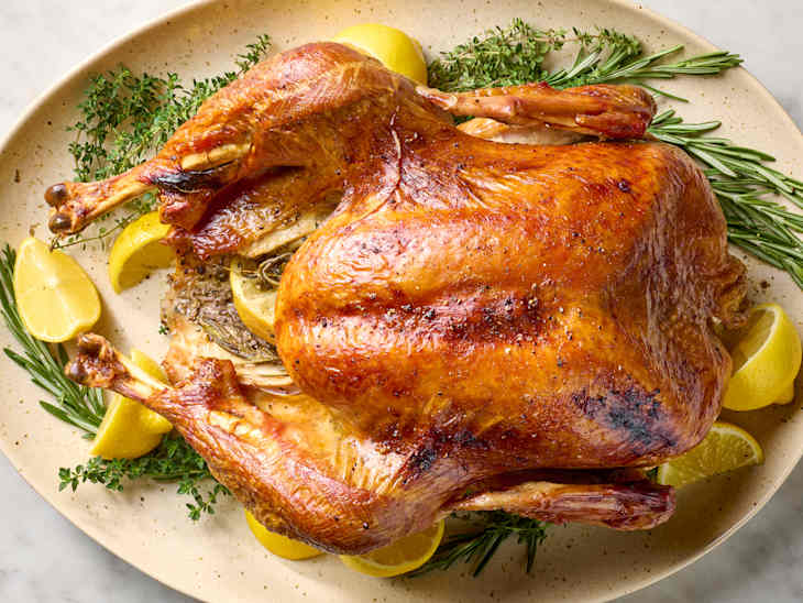 overhead shot of cooked turkey on a platter with herbs and lemon