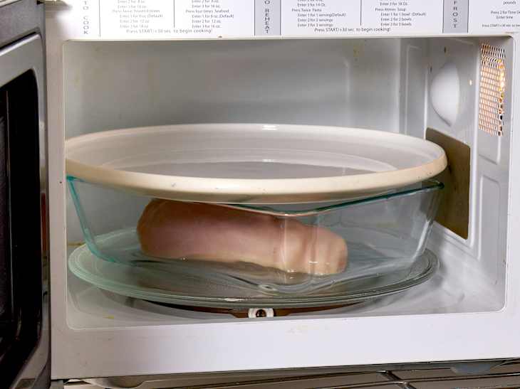 A chicken breast getting defrosted in a microwave