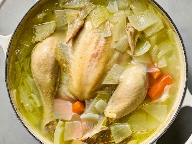 overhead shot of a whole chicken in a pot with carrots, onion and celery