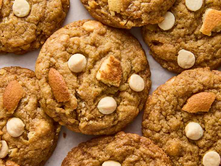 Chewy cookies with white chocolate chips and pieces of golden brown cookie on a parchment surface.