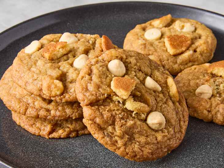 Stack of freshly baked cookies with white chocolate chips and pieces of cookie on a dark plate.