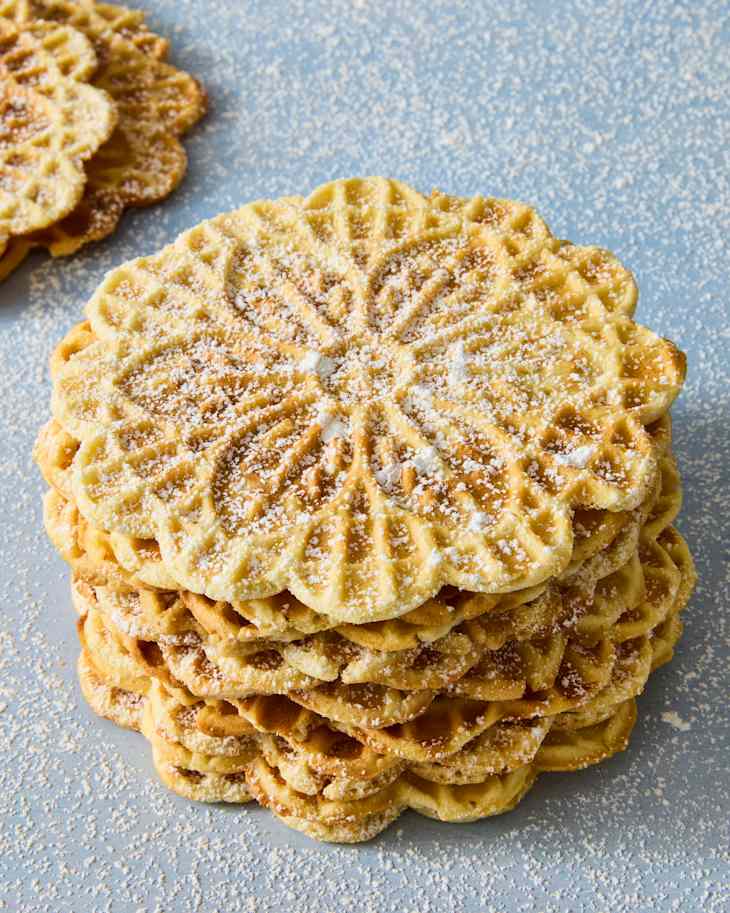Stack of decorative waffle cookies dusted with powdered sugar on a light blue surface.
