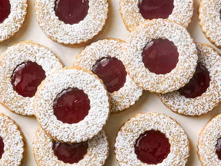 Round cookies with a powdered sugar rim and a red jam center, arranged closely together.
