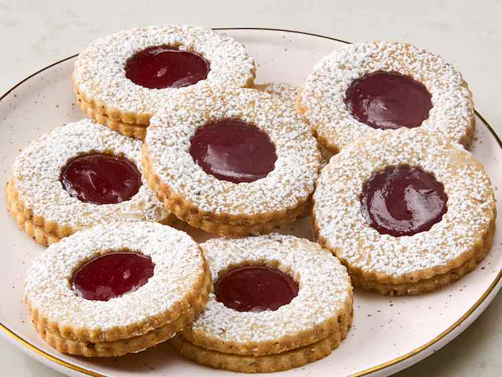 Round cookies with a jam center, dusted with powdered sugar, arranged on a pale pink plate.