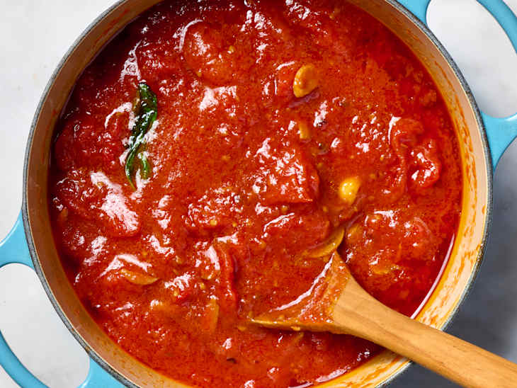 overhead shot marinara in a large pot with a wooden spoon in it
