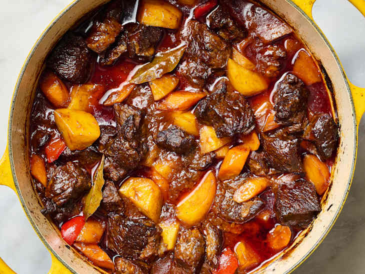 Savory beef stew with chunks of potatoes, red peppers, in a yellow dutch oven