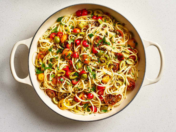 Spaghetti with cherry tomatoes, olives, capers, and parsley in a white pot.