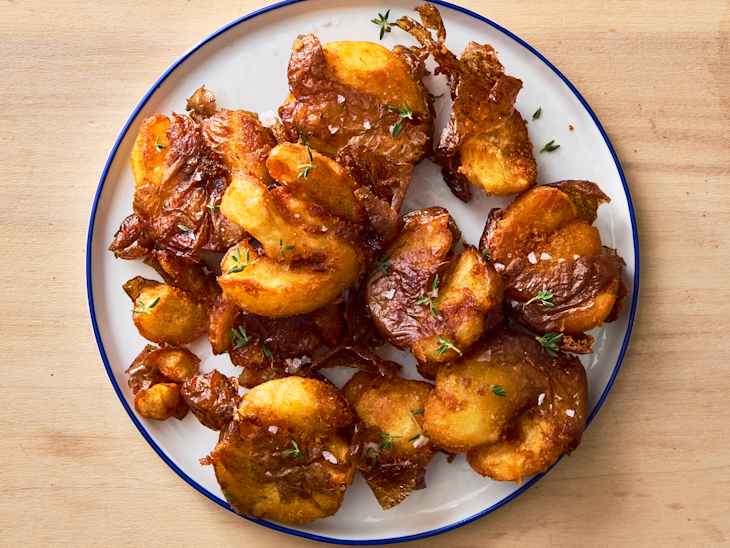 Crispy golden-brown fried potatoes garnished with fresh thyme on a white plate.