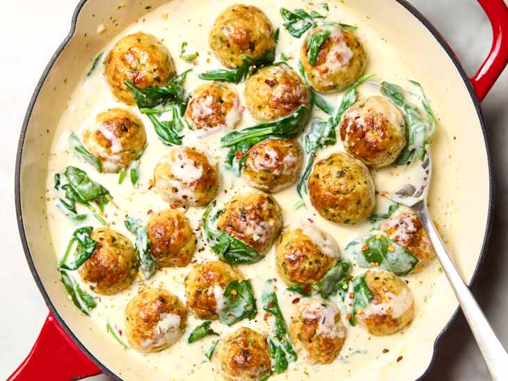 overhead shot of parmesan chicken meatballs with creamy spinach in a red cast iron pan
