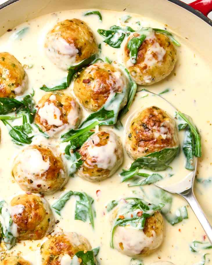 overhead shot of parmesan chicken meatballs with creamy spinach in a red cast iron pan