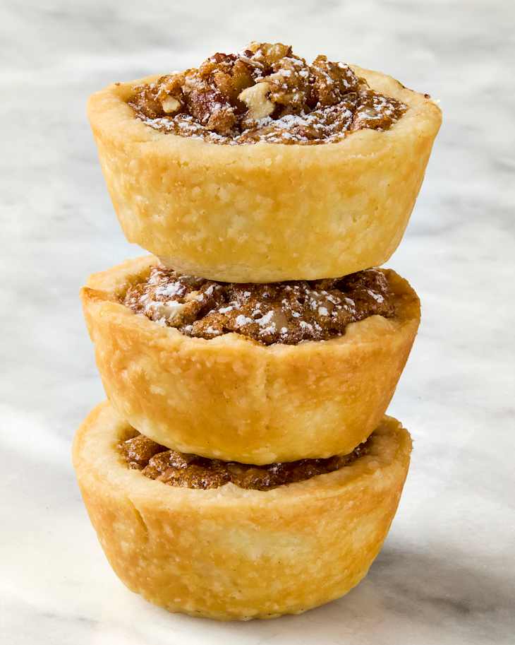 Three stacked pastry cups filled with a sweet, crumbly mixture, dusted with powdered sugar.