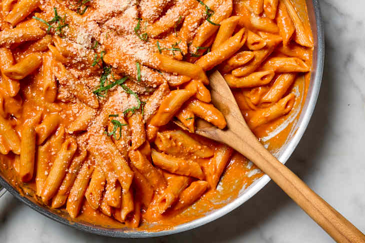 overhead shot of penne alla vodka in a pan with a wooden spoon resting in it.