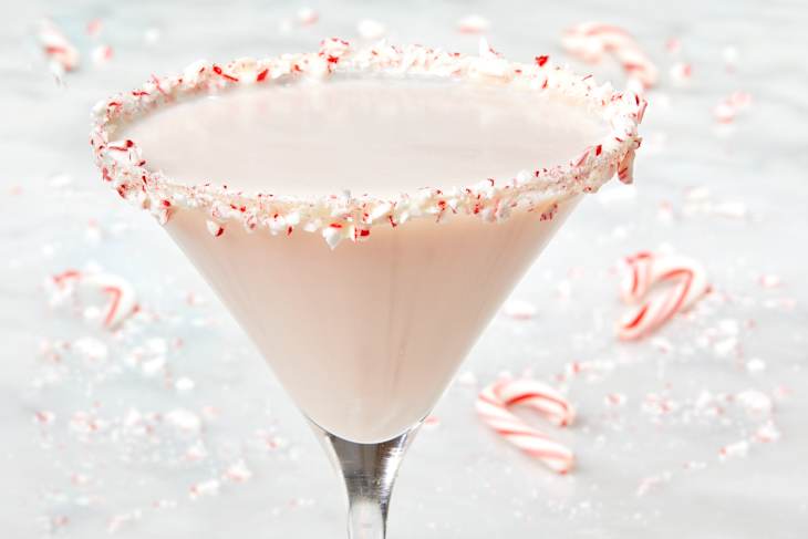 Close up head on shot of a peppermint martini with a candy cane rim and broken candy cane pieces in the background of the shot.