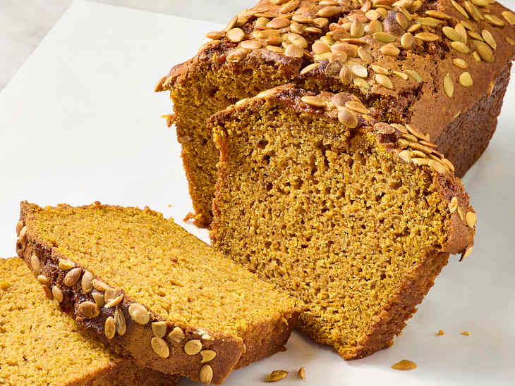 Sliced pumpkin bread topped with pumpkin seeds, showcasing a moist texture and golden color.